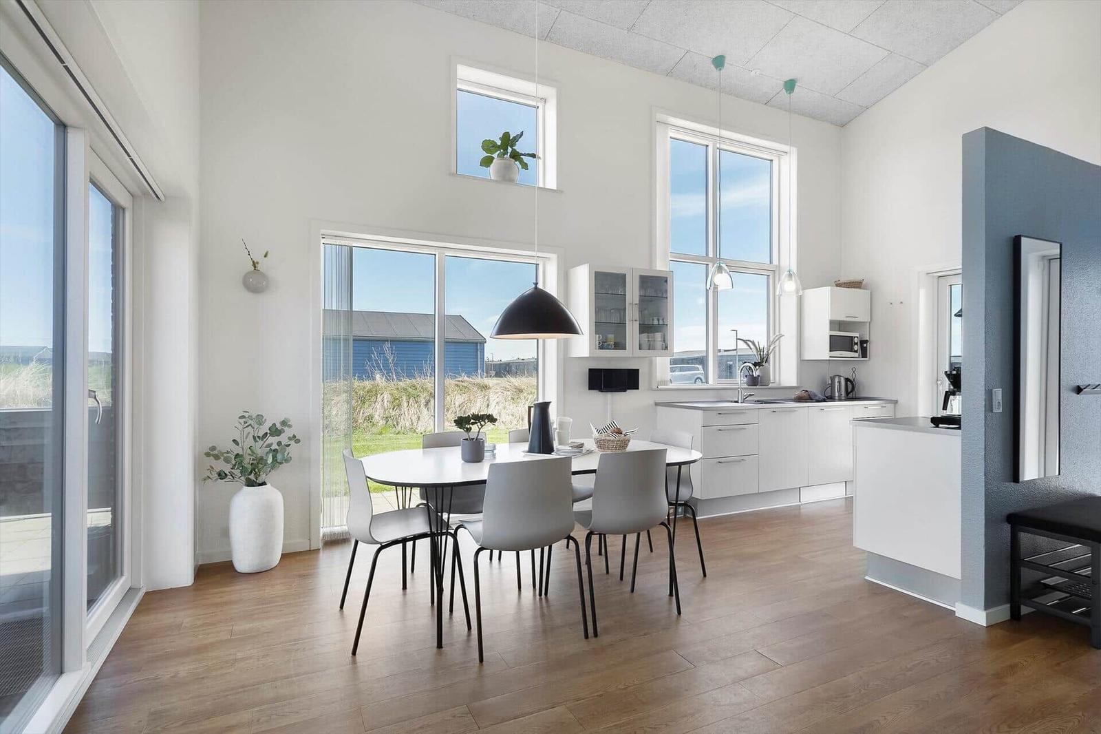 Moderne Küche mit Esstisch, großen Fenstern und Holzboden. Blick auf Außenbereich.