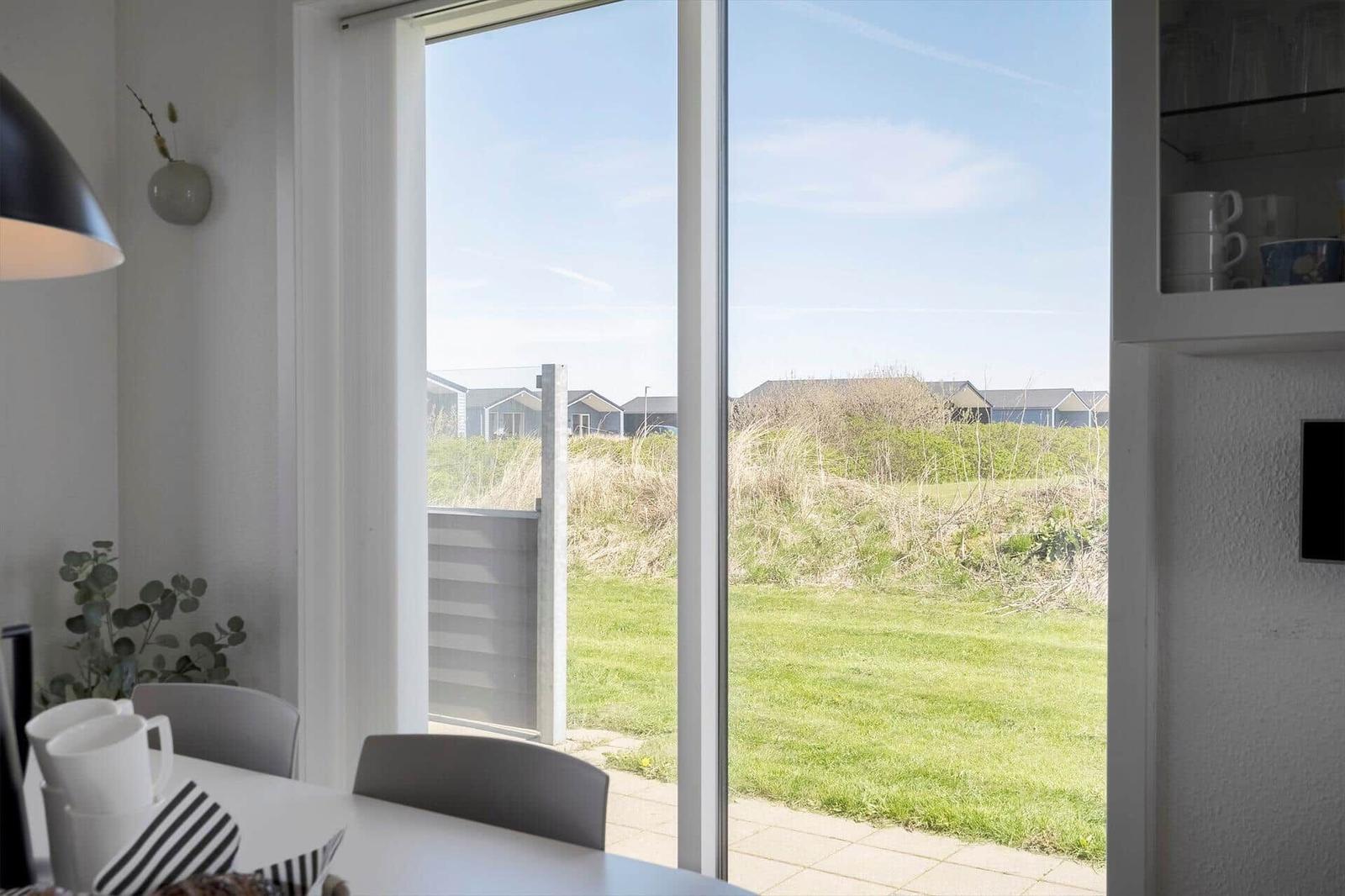 Durch das Fenster blickt man auf einen grünen Rasen und Strandhäuser im Hintergrund.