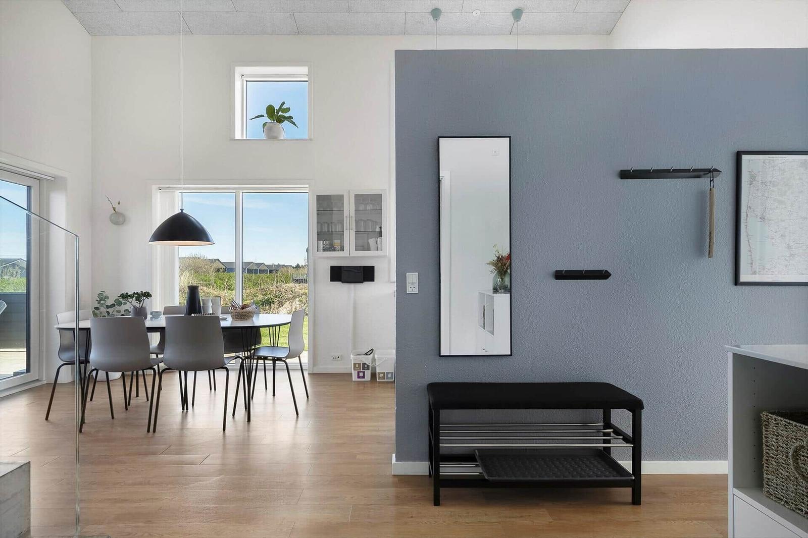 Eingangsbereich mit Spiegel, Hocker und Wandhalterungen. Im Hintergrund Essbereich mit Tisch und Stühlen.