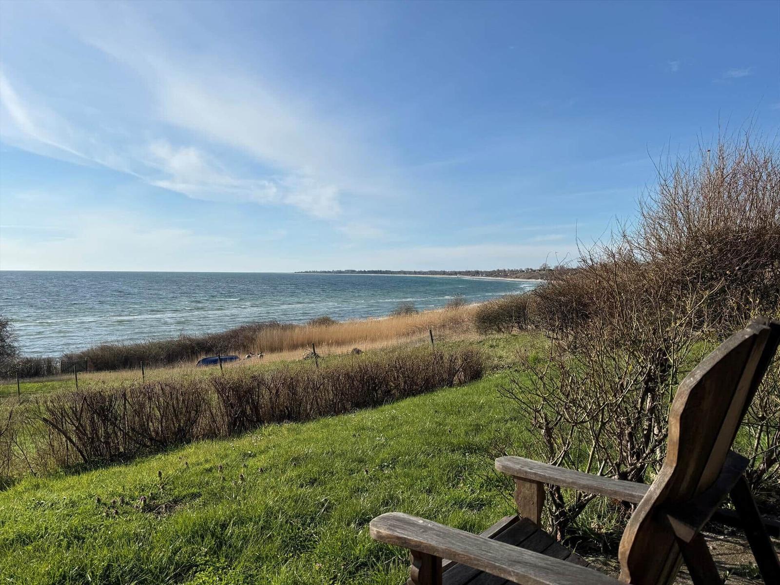 Holzstuhl auf grünem Rasen mit Blick auf das Meer und Strand.