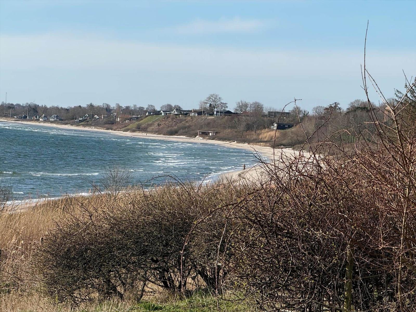 Strand mit Wellen, Dünen und Häusern im Hintergrund.