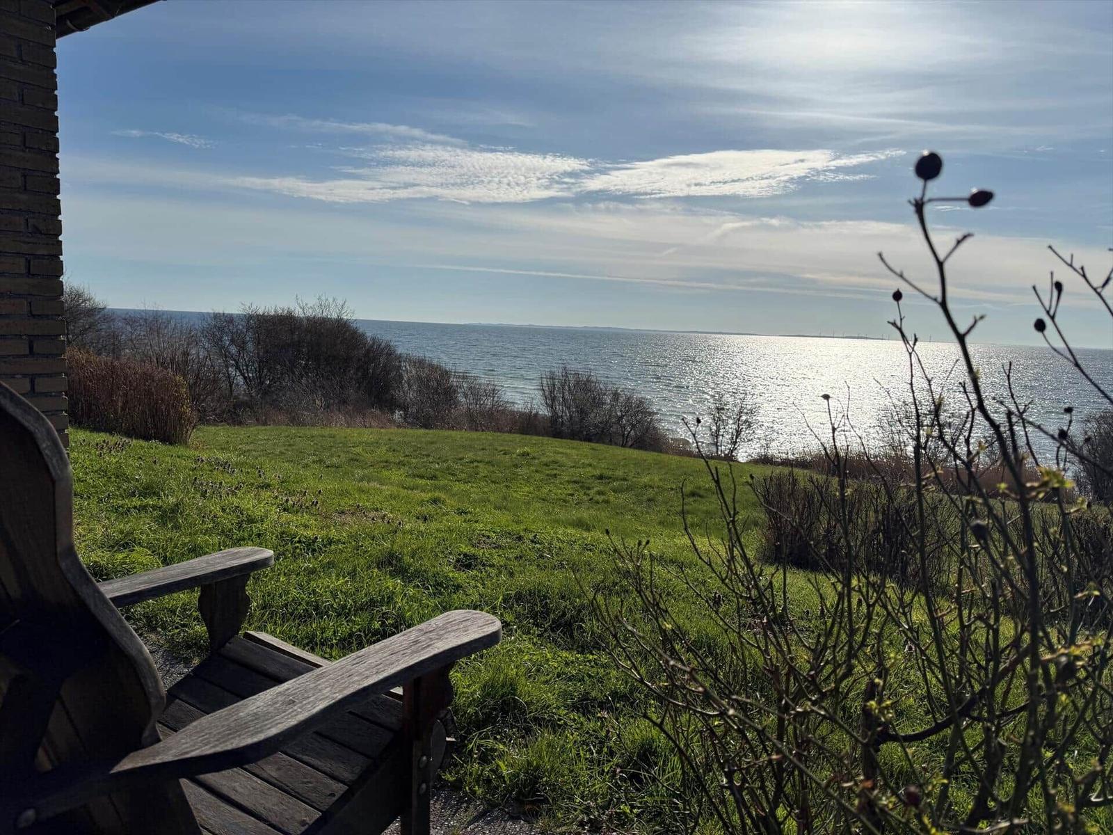 Holzstuhl auf Terrasse mit Blick auf grünen Hang und Meer.