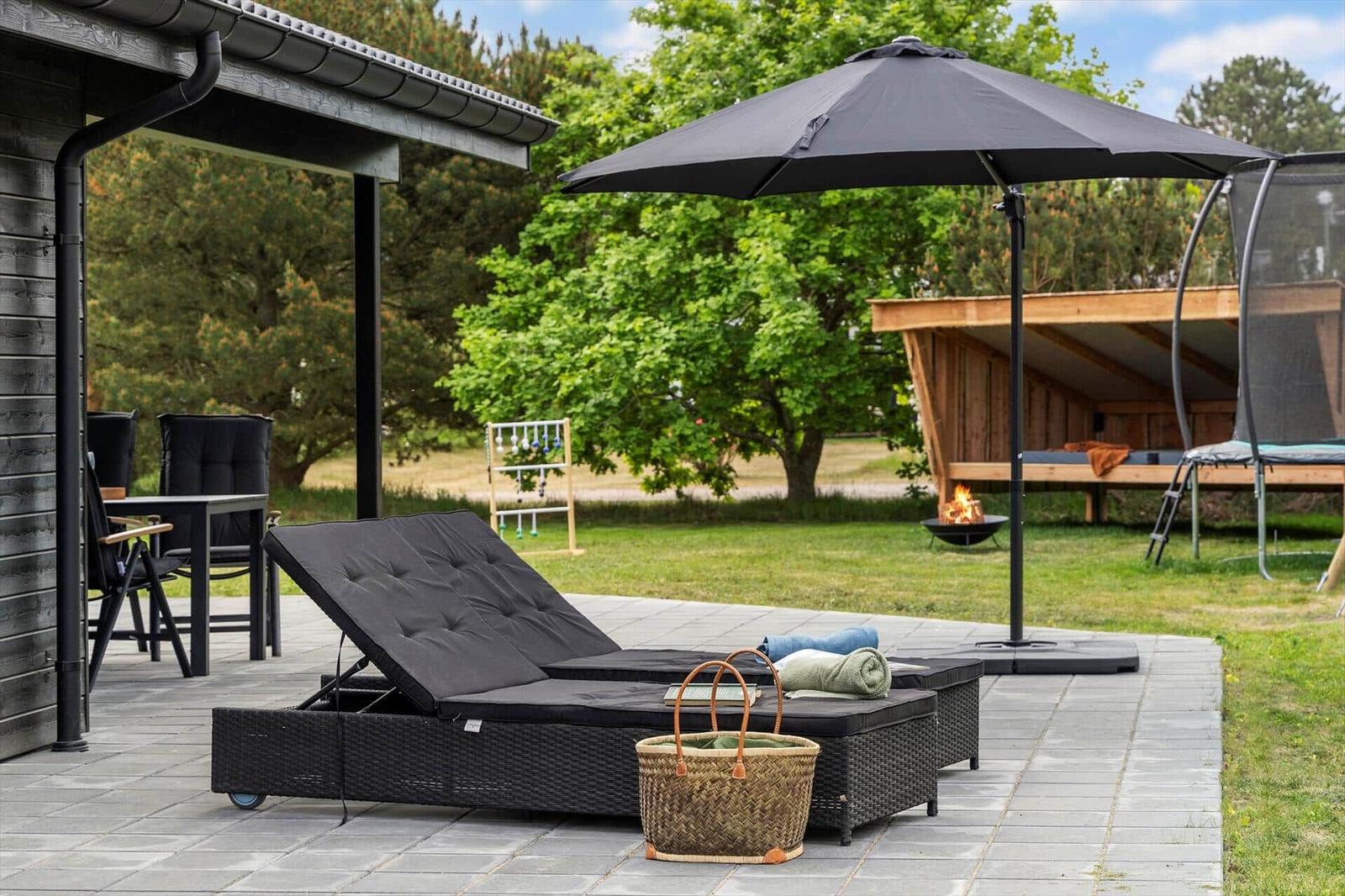 Terrace with lounge chair, umbrella, and fire pit. Background: lawn, tree, and trampoline.