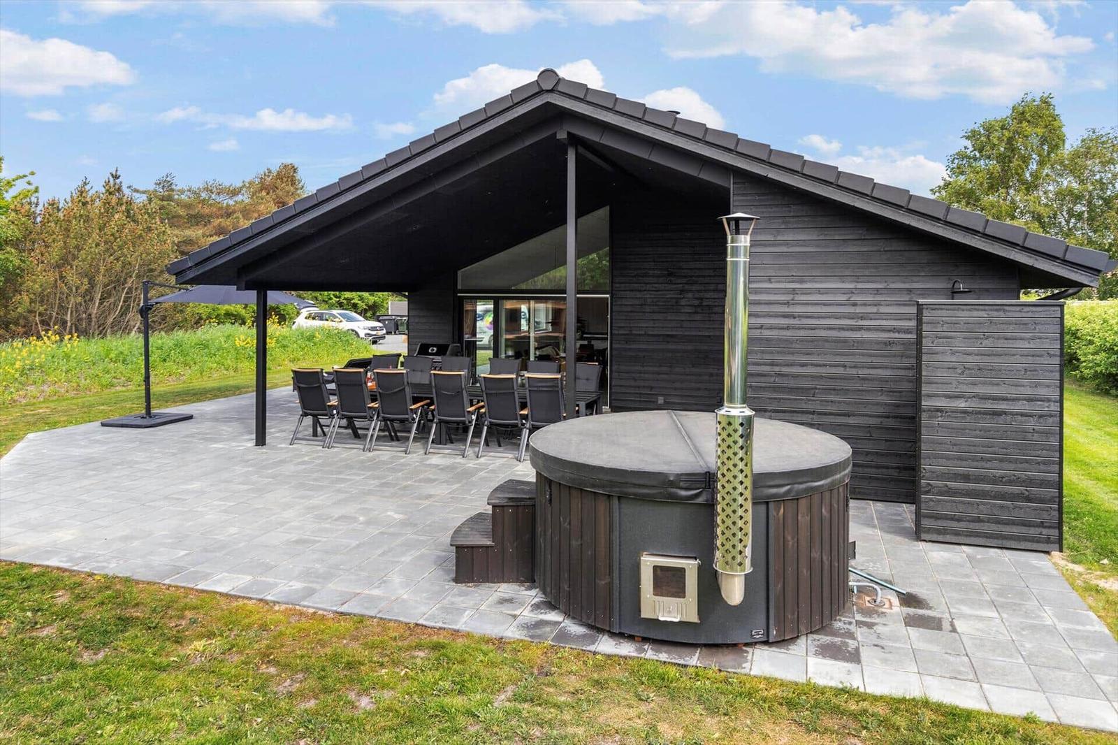 Modern wooden cabin with terrace, grill, and outdoor hot tub.