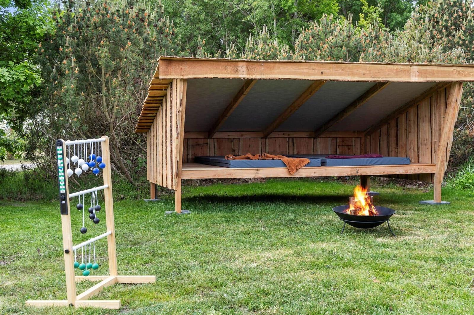 Wooden structure with mattresses, fire pit, and game equipment in the garden.