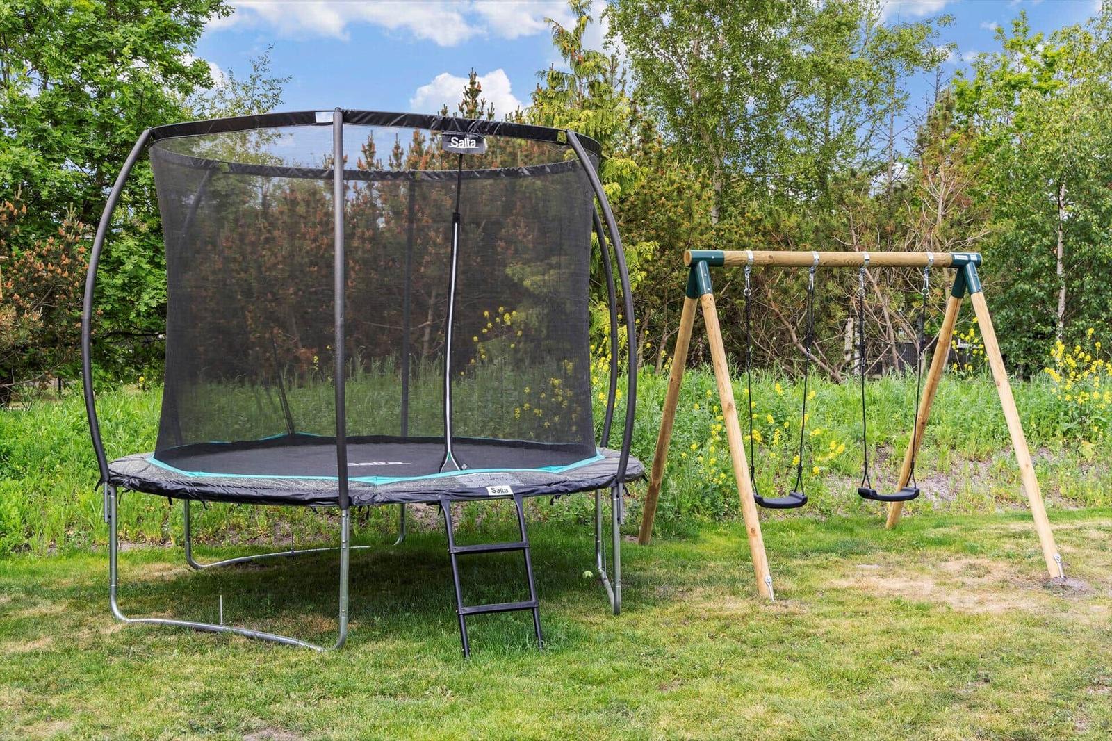 A trampoline with safety net and a swing in the garden.