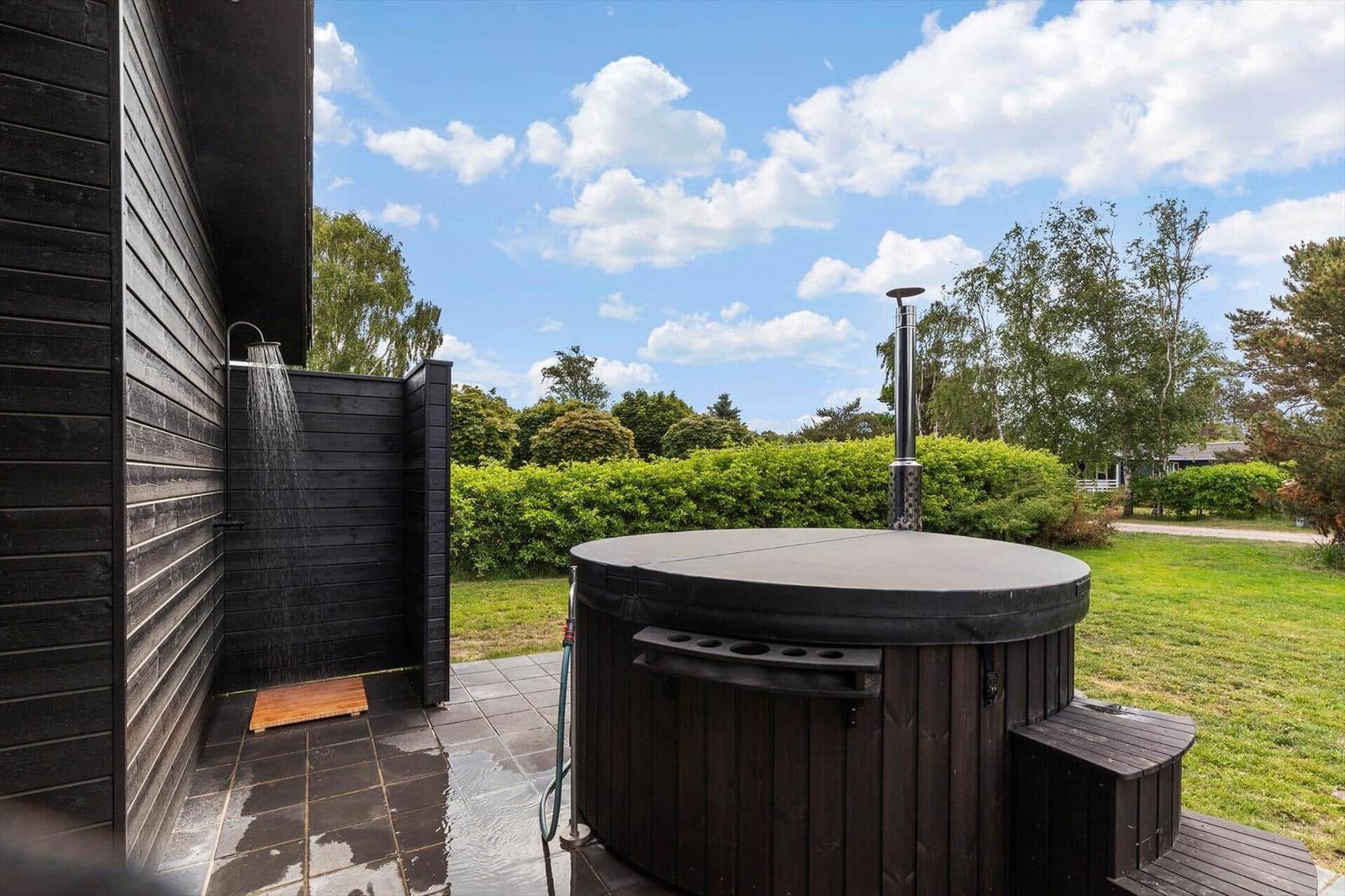 Outdoor hot tub with shower and grill, surrounded by greenery and trees.