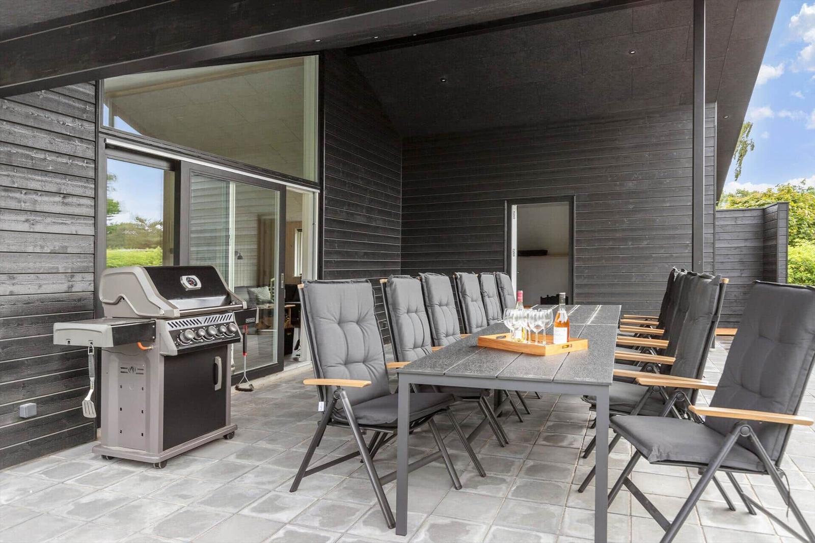 Terrace with grill, dining table, and chairs. Background: house with glass facade.
