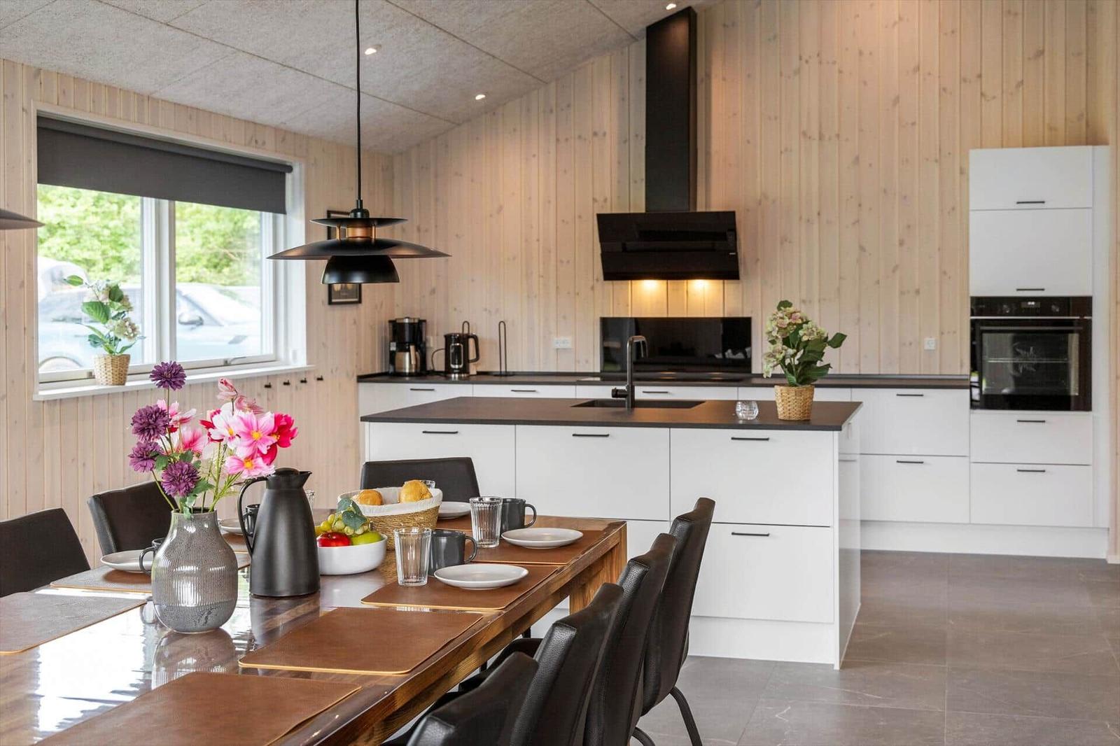 Modern kitchen with dining area, wood paneling, and black appliances.