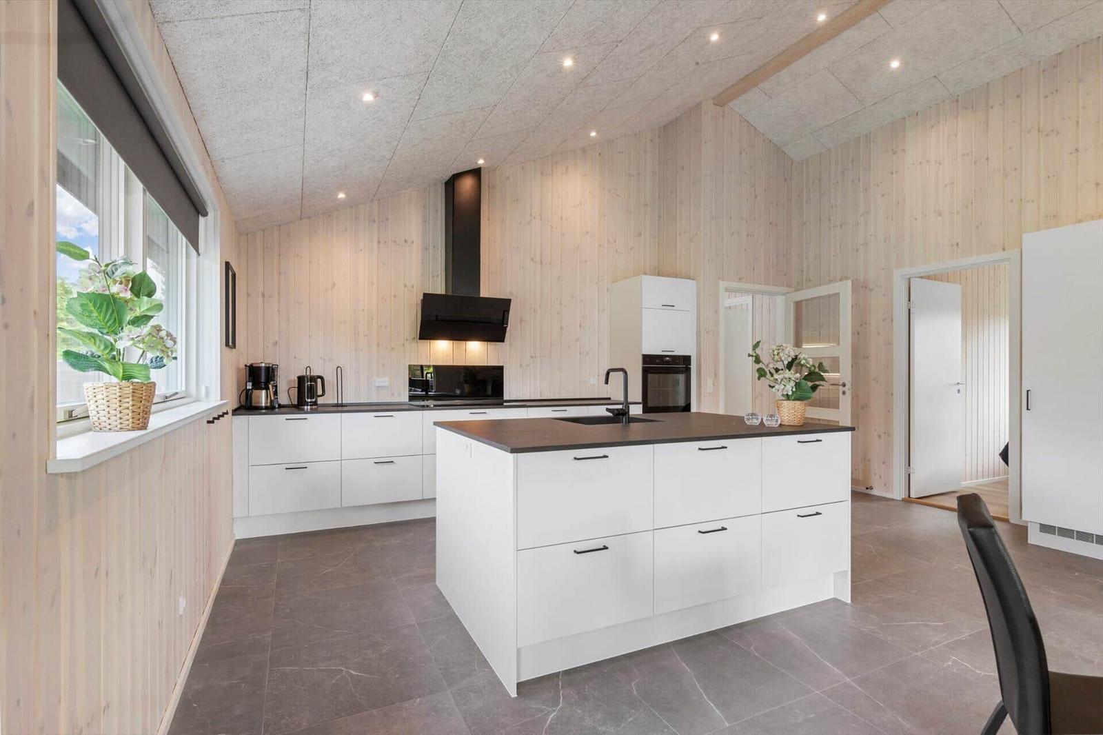 Kitchen with white cabinets, dark worktop, and wood paneling.