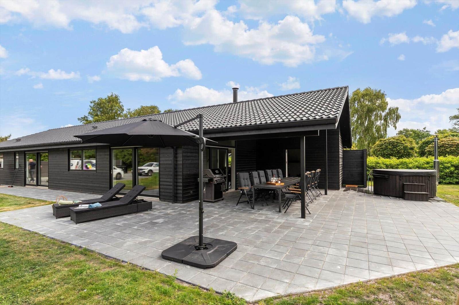 Modern villa with large patio, grill, loungers, and hot tub in the garden.