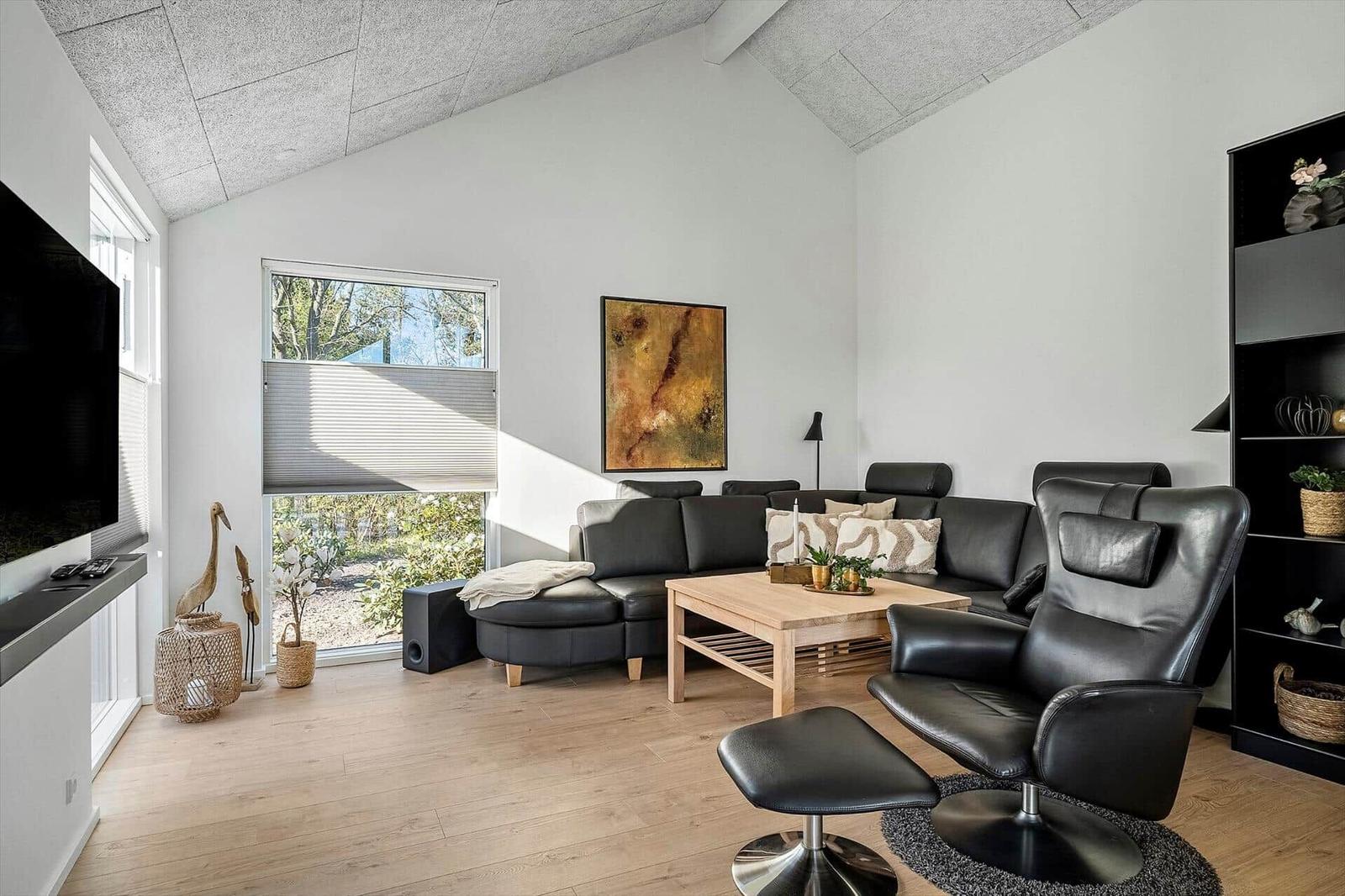 Wohnzimmer mit schwarzen Ledermöbeln, Holztisch und Fensterblick auf Garten.
