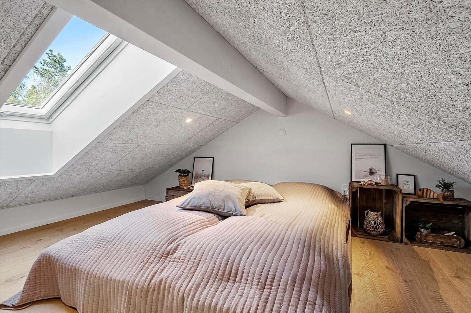 Schlafzimmer mit Dachschrägen, Dachfenster und Holzboden. Bett mit Bettwäsche und Nachttische.