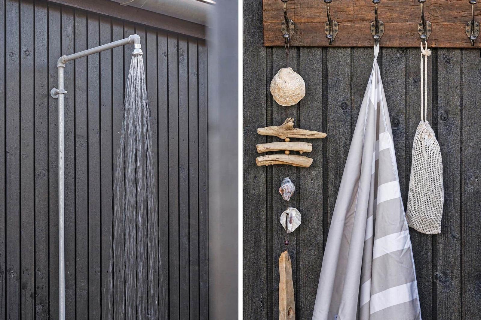 Außendusche mit Wasserstrahl und hölzerner Wand mit Haken für Handtuch und Seetang.