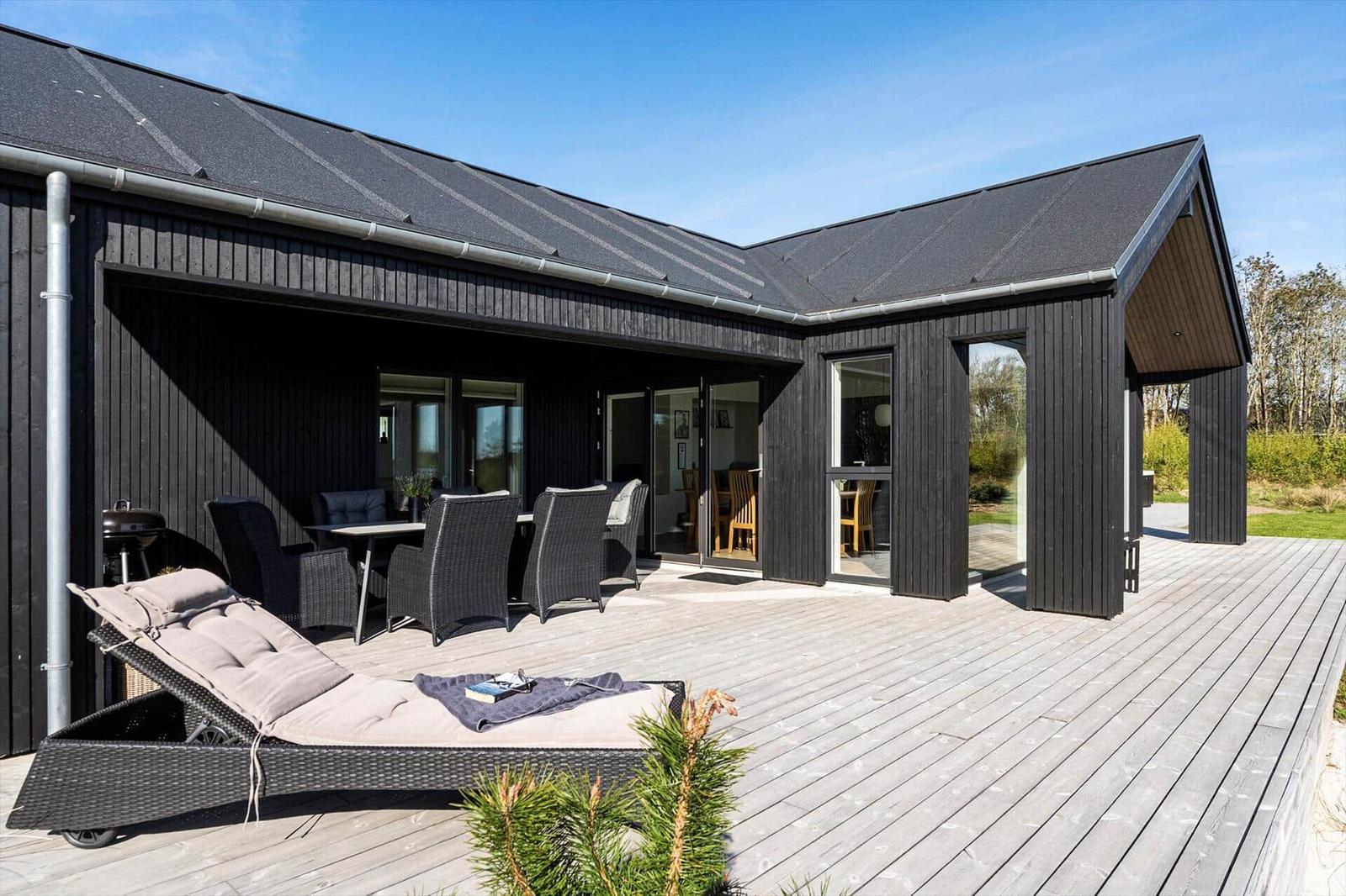 Moderne Villa mit Terrasse, Liegestuhl und Grill. Durchgehendes Glas ermöglicht Blick ins Haus.