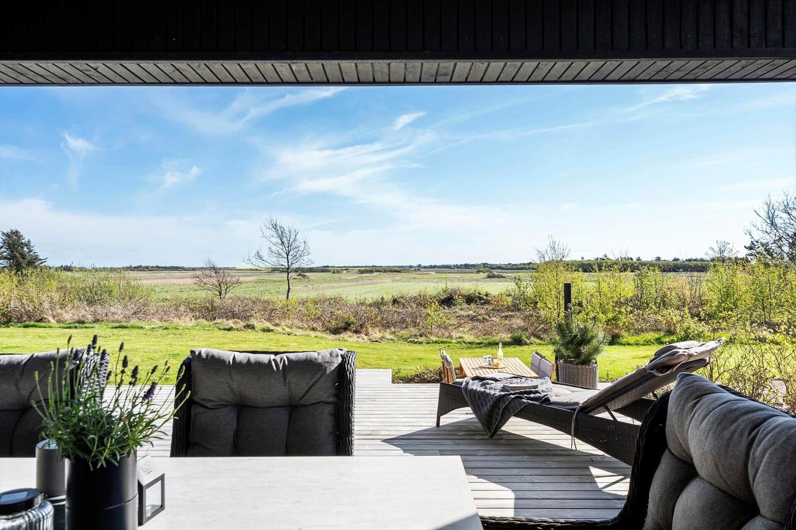 Terrasse mit Sitzgelegenheiten und Blick auf grünes Feld.