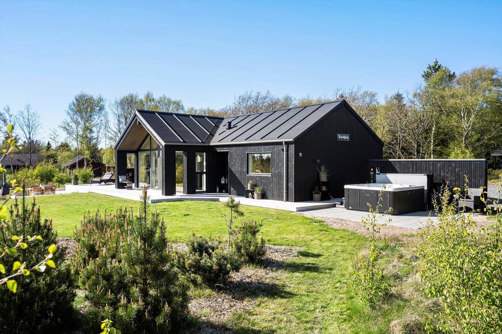 Moderne schwarze Hütte mit Whirlpool und Garten. Umgeben von Bäumen und Gras.