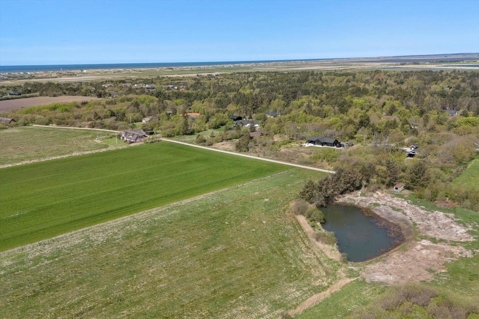 Landschaftsaufnahme mit Wiesen, Wald und einem See. Im Hintergrund ist das Meer zu sehen.