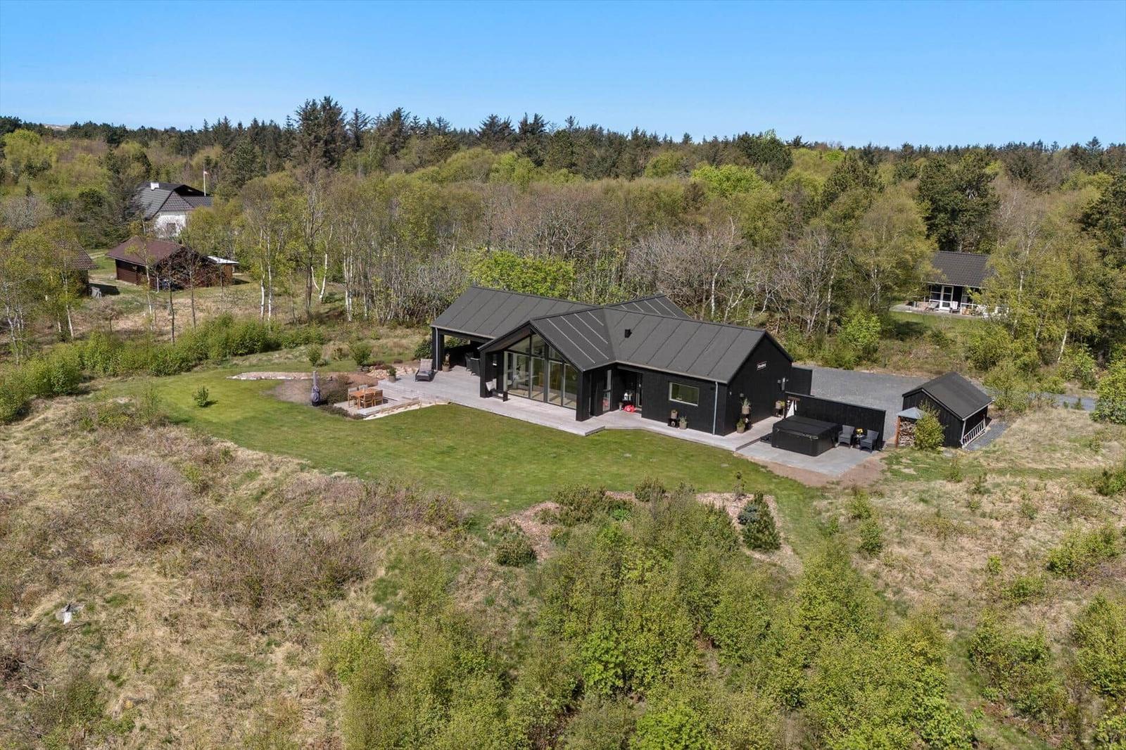 Moderne schwarze Villa mit großem Garten und Terrasse in Waldnähe.
