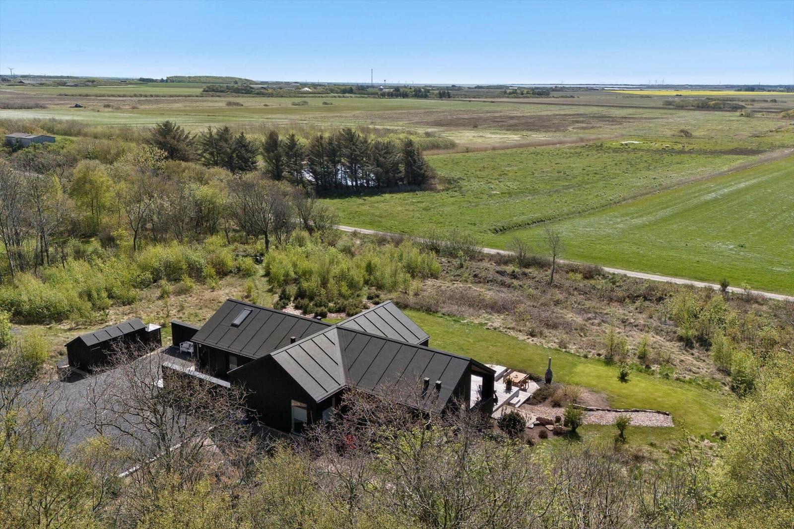 Moderne Holzhütte mit Terrasse im Grünen, umgeben von Feldern und Bäumen.
