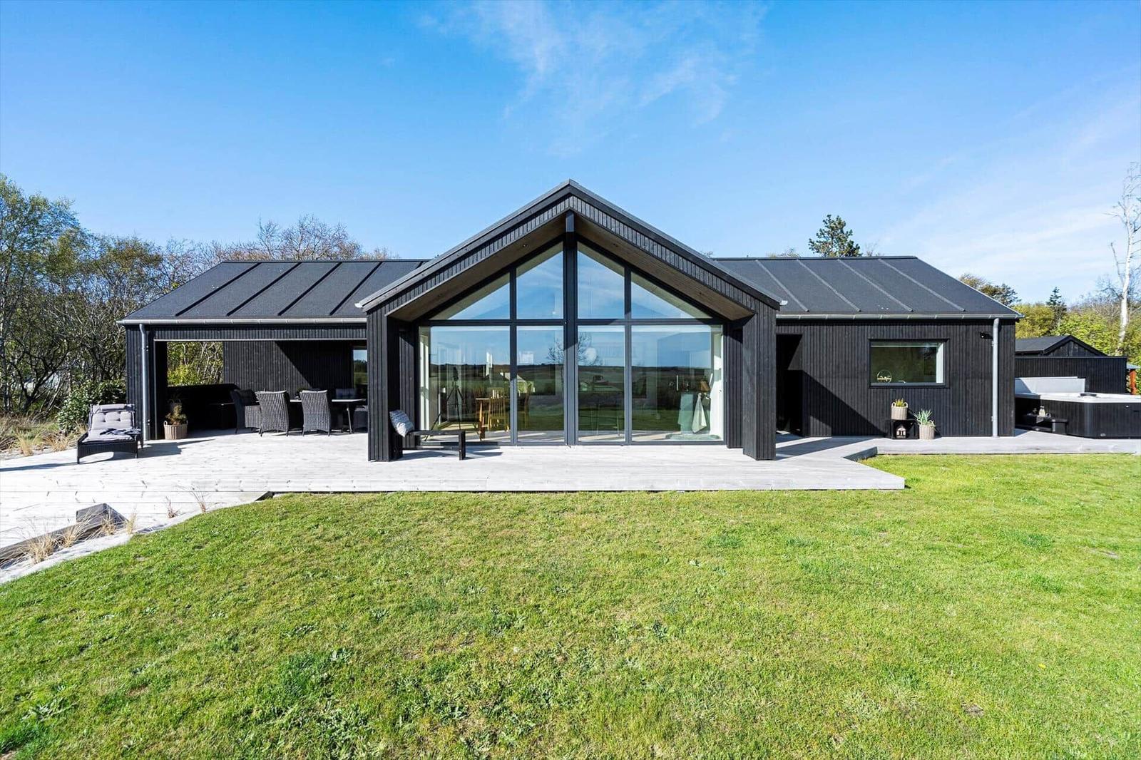 Moderne Villa mit großem Glasbereich und Terrasse. Grünfläche und Außensitzgelegenheiten.