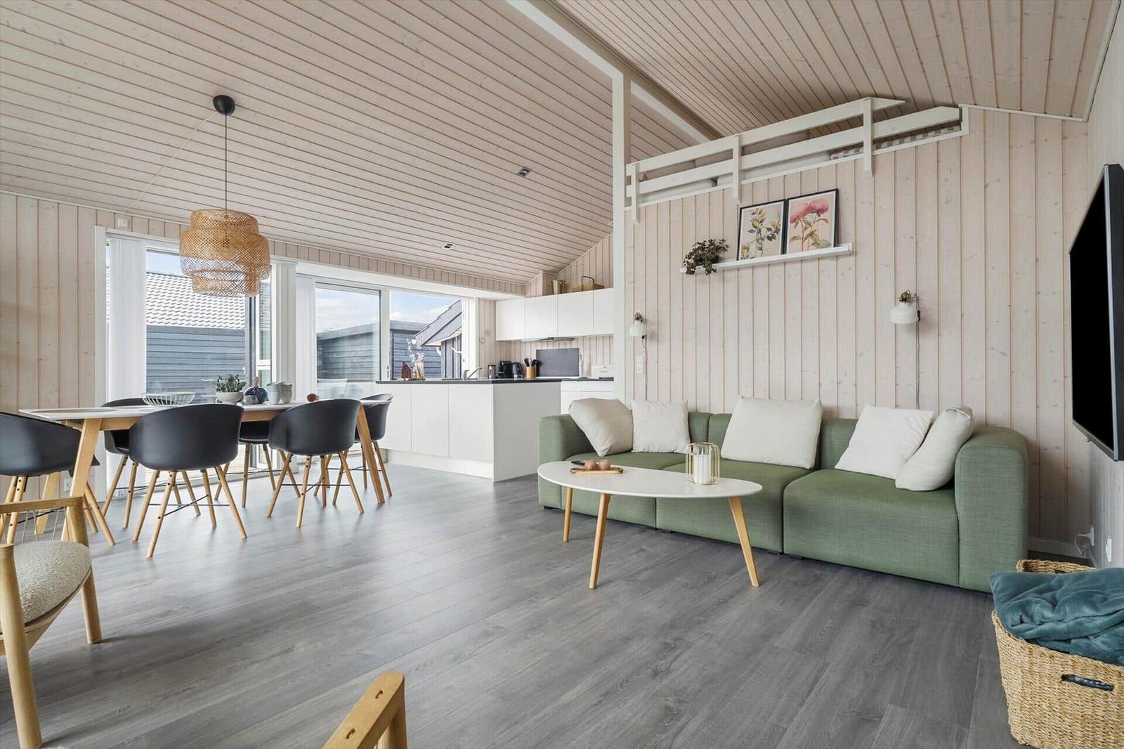 Wohnbereich mit grünem Sofa, Esstisch und Küchenzeile unter Holzdecke.