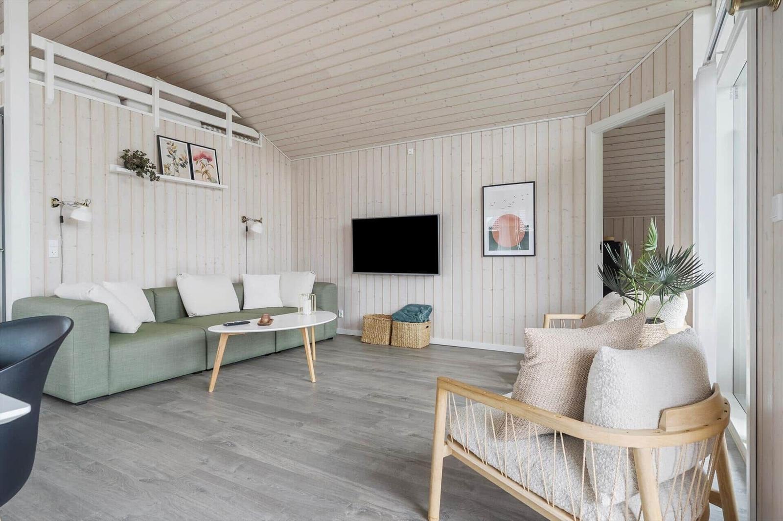 Wohnzimmer mit grünem Sofa, Holzstuhl und Fernseher an der Wand.