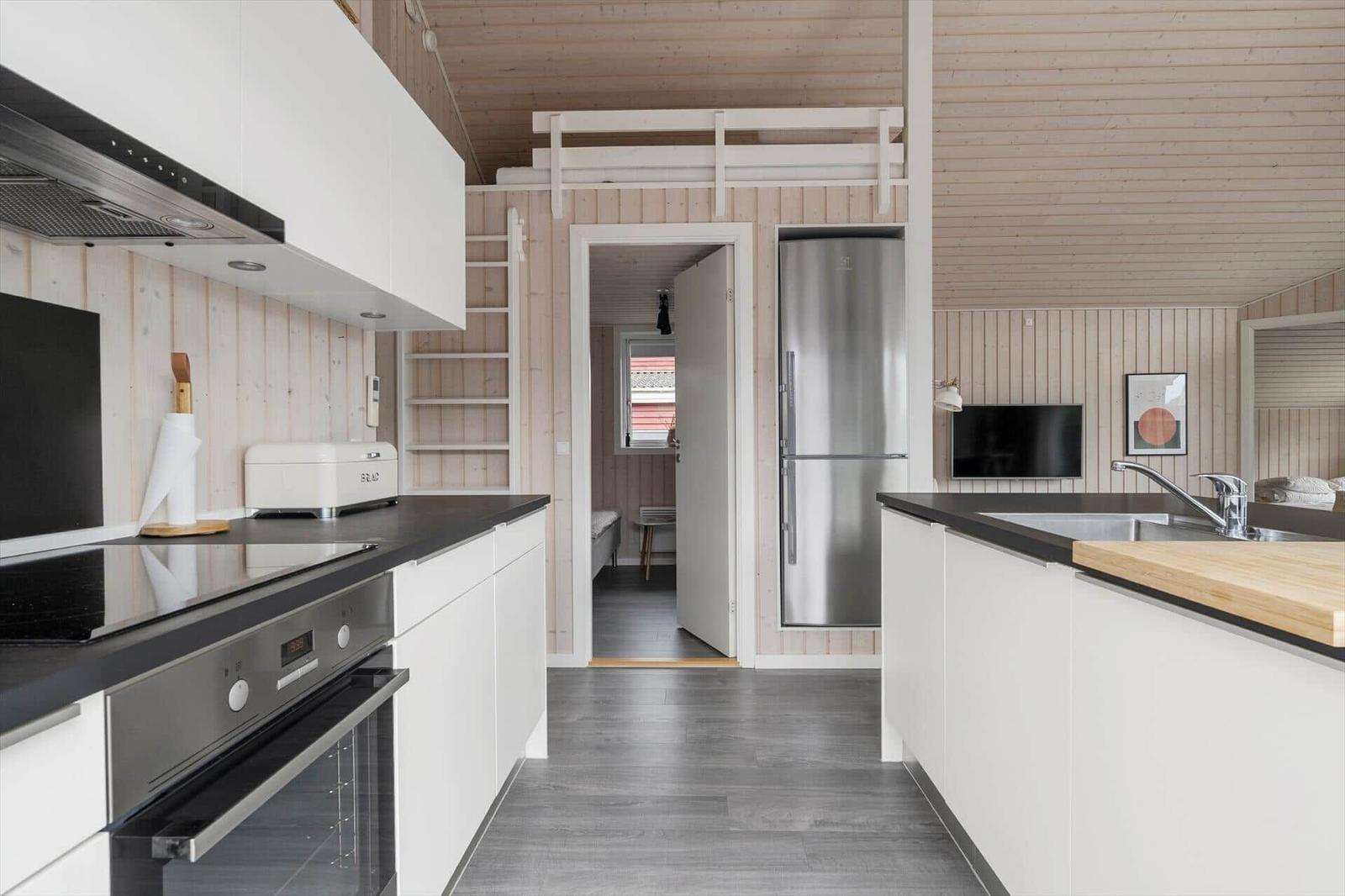 Küche mit Edelstahlgeräten und Holzwandverkleidung. Obergeschoss mit Schlafbereich.