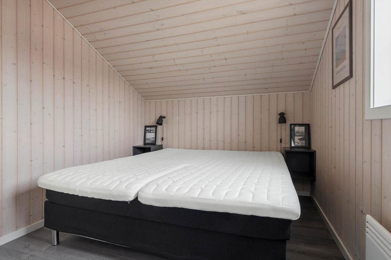 Schlafzimmer mit Holzwänden und einem Bett mit weißer Matratze.