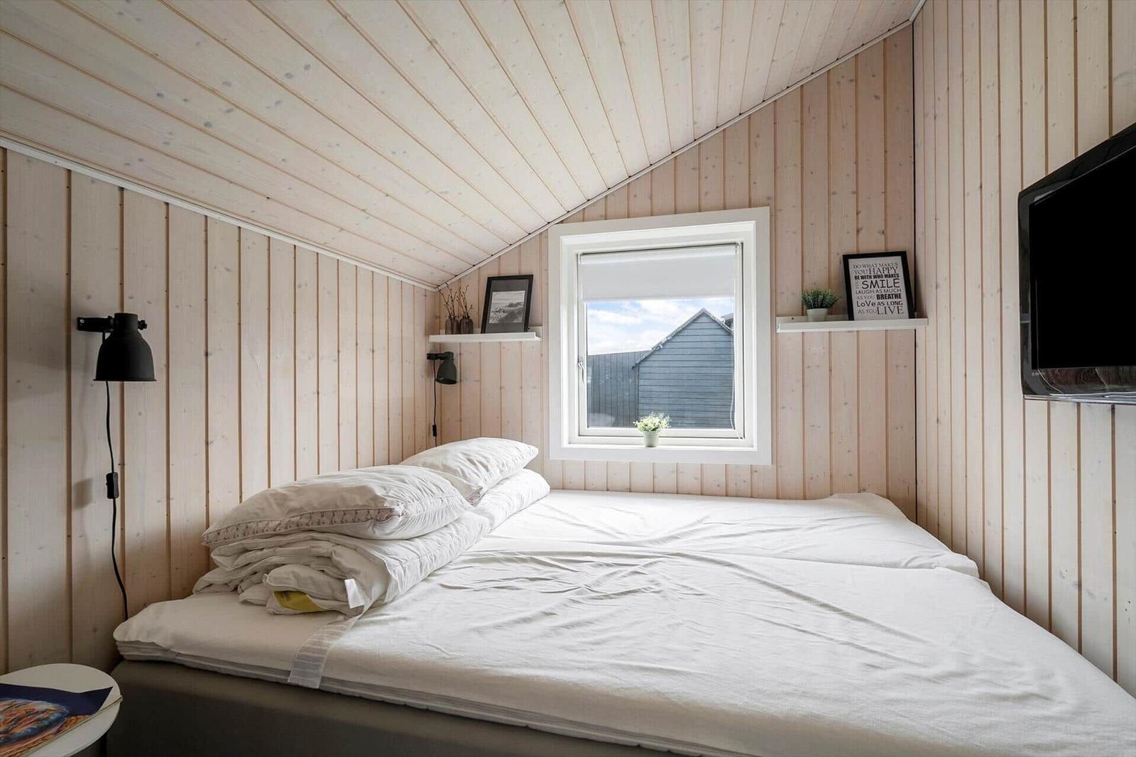 Schlafzimmer mit Bett, Fenster und Holzwandverkleidung.