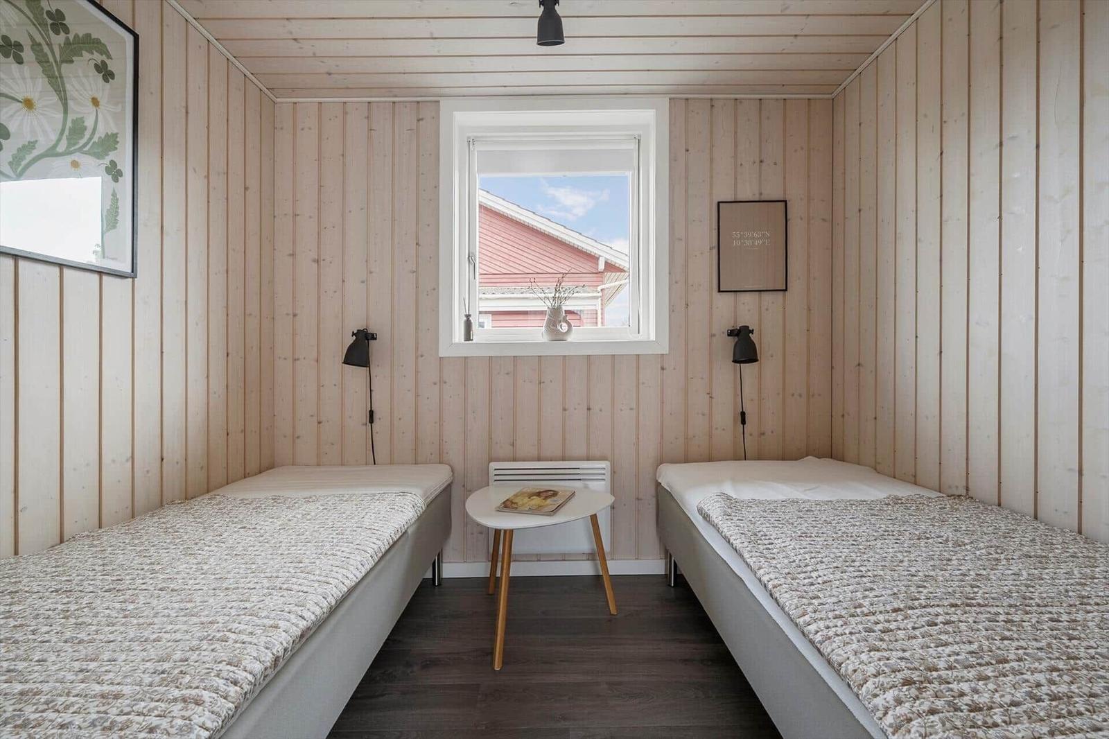 Zwei Einzelbetten mit Decken, Wandbild und Fenster mit Blick auf ein rotes Haus.