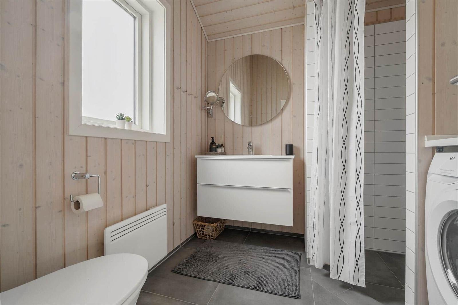 Badezimmer mit Holzwand, Waschbecken, Dusche und Waschmaschine.