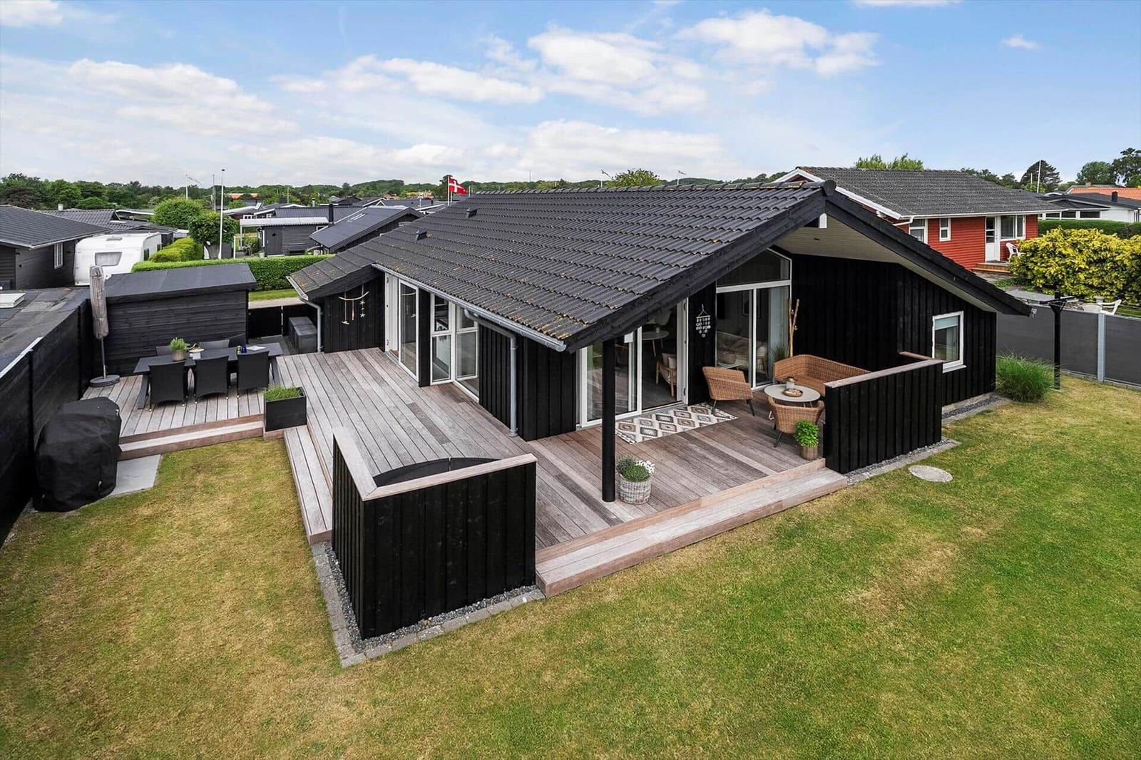 Schwarzes Holzhaus mit Terrasse und Garten. Große Fensterfront. Möbel auf der Veranda.