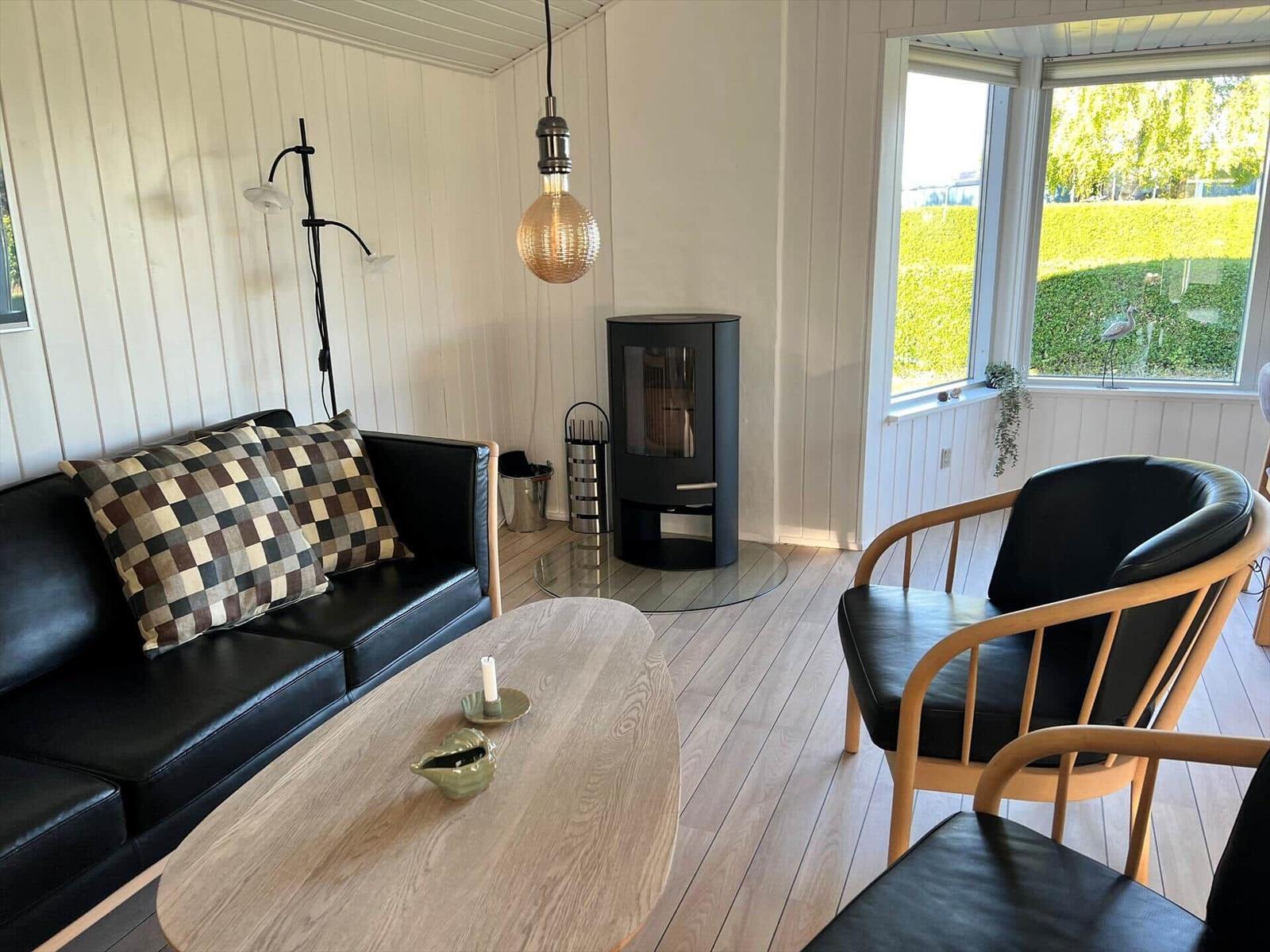 Wohnzimmer mit Sofa, Stuhl, Kamin und Tisch. Durch Fenster Blick auf Grünfläche.