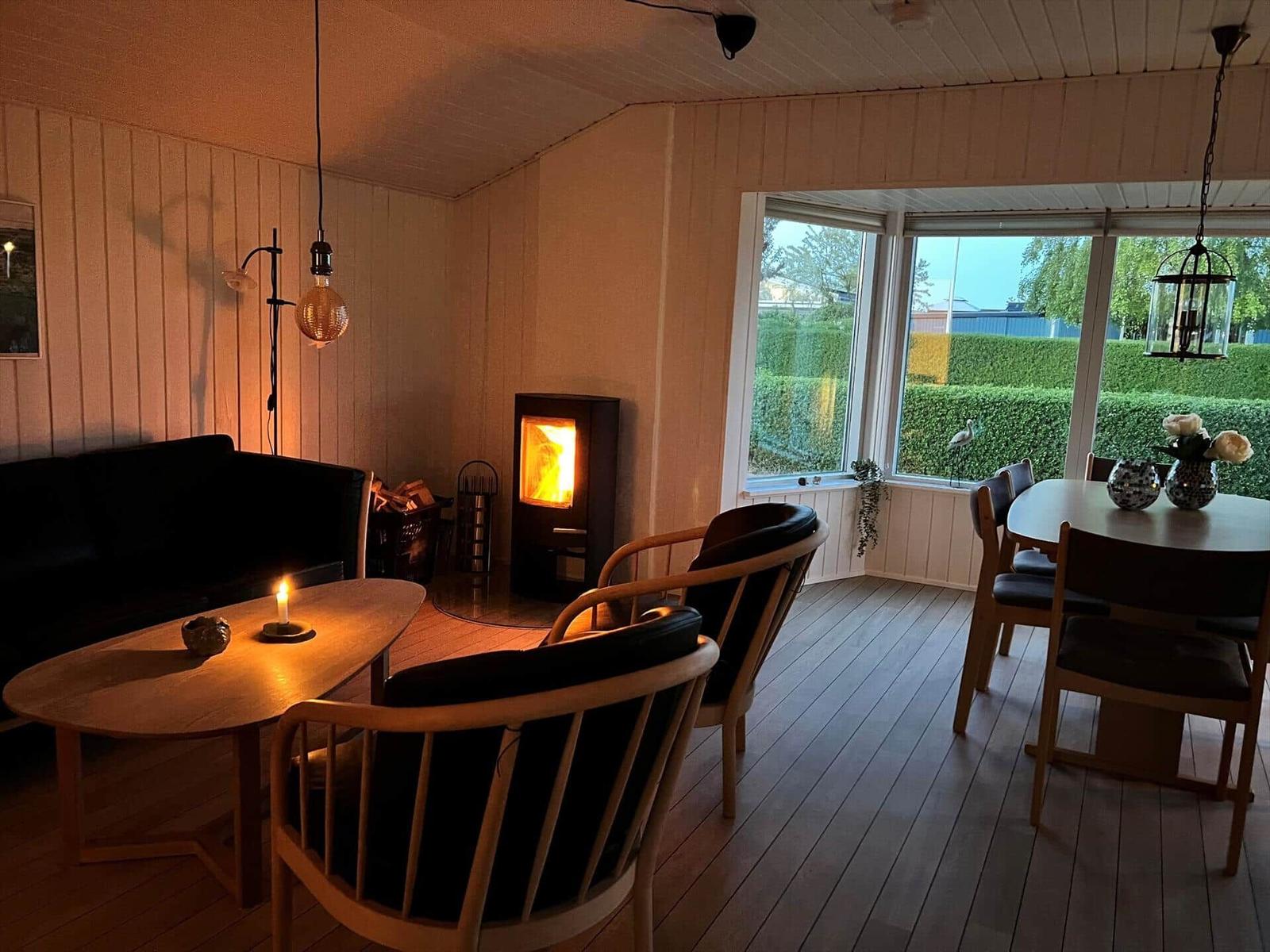 Wohn- und Essbereich mit Kamin, Holzfußboden und großem Fenster zur grünen Außenansicht.