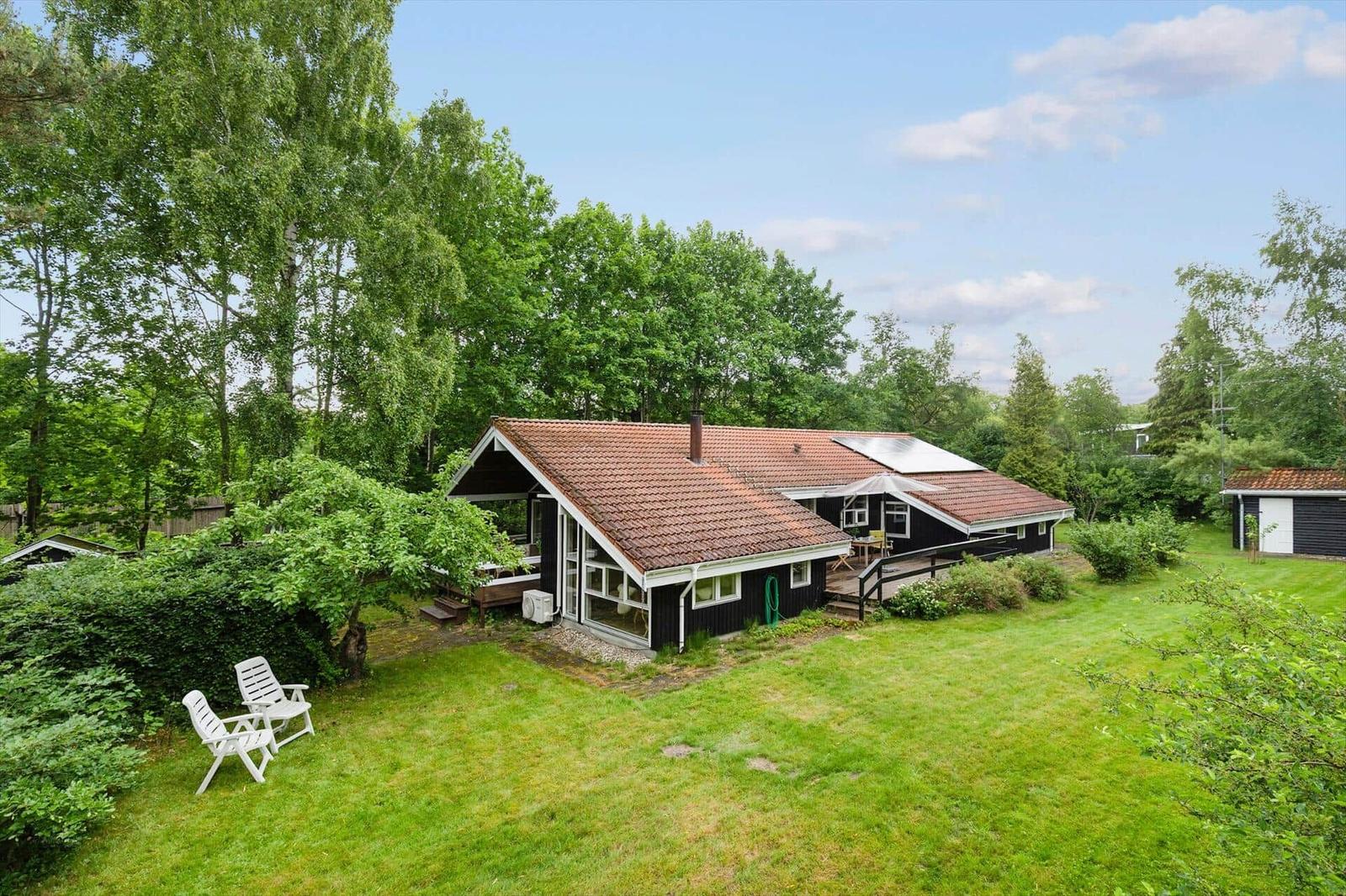 A house with a red roof and garden. White chairs are outside.