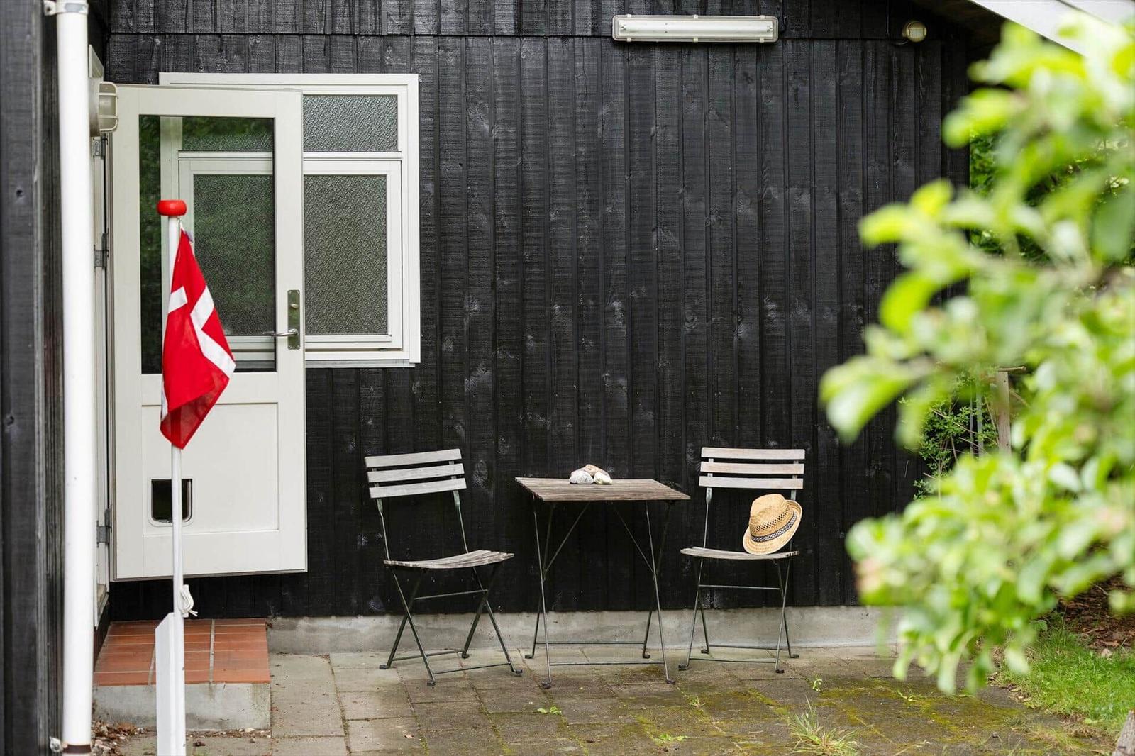 Backyard with table, two chairs, and Danish flag in front of black wooden house.