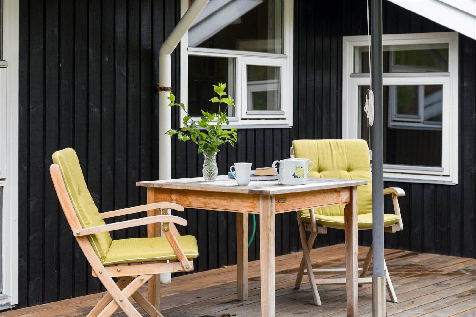 Bright green seating surrounds a wooden table on a terrace in front of a black-clad house.