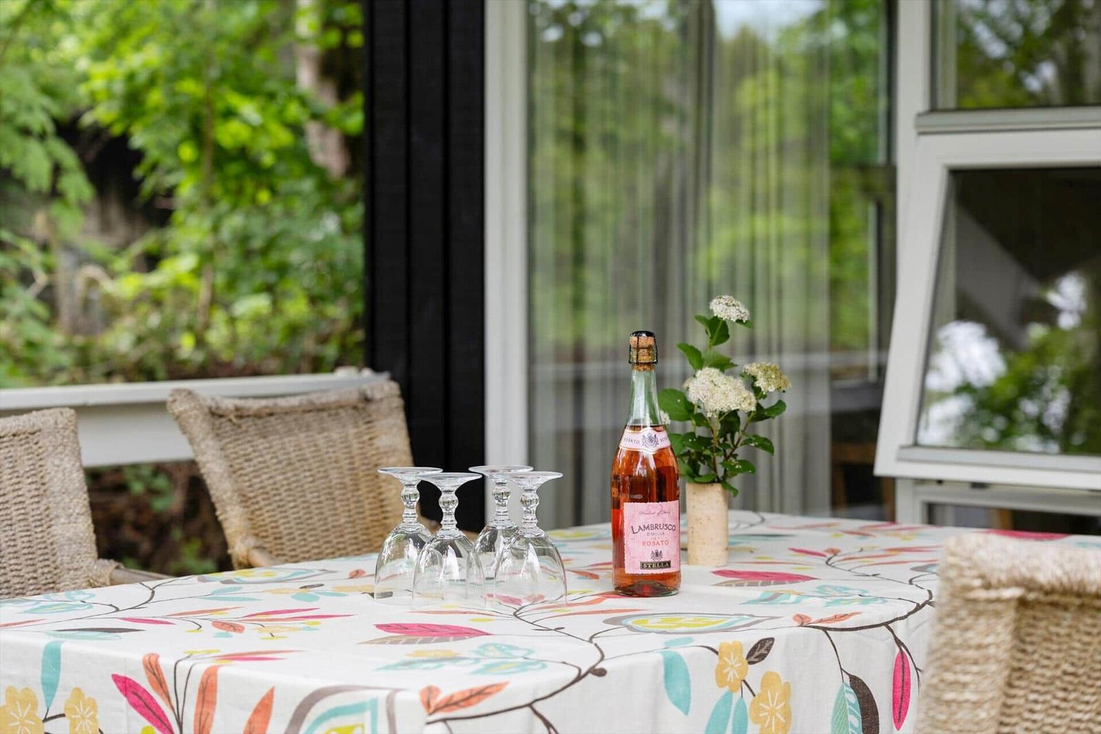 Table with floral tablecloth, wine bottle, and glasses outdoors.