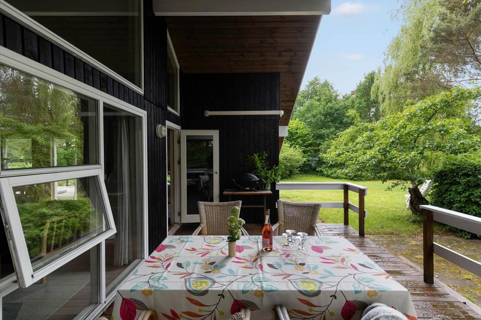 Deck with table, chairs, and grill. View of green lawn and trees.