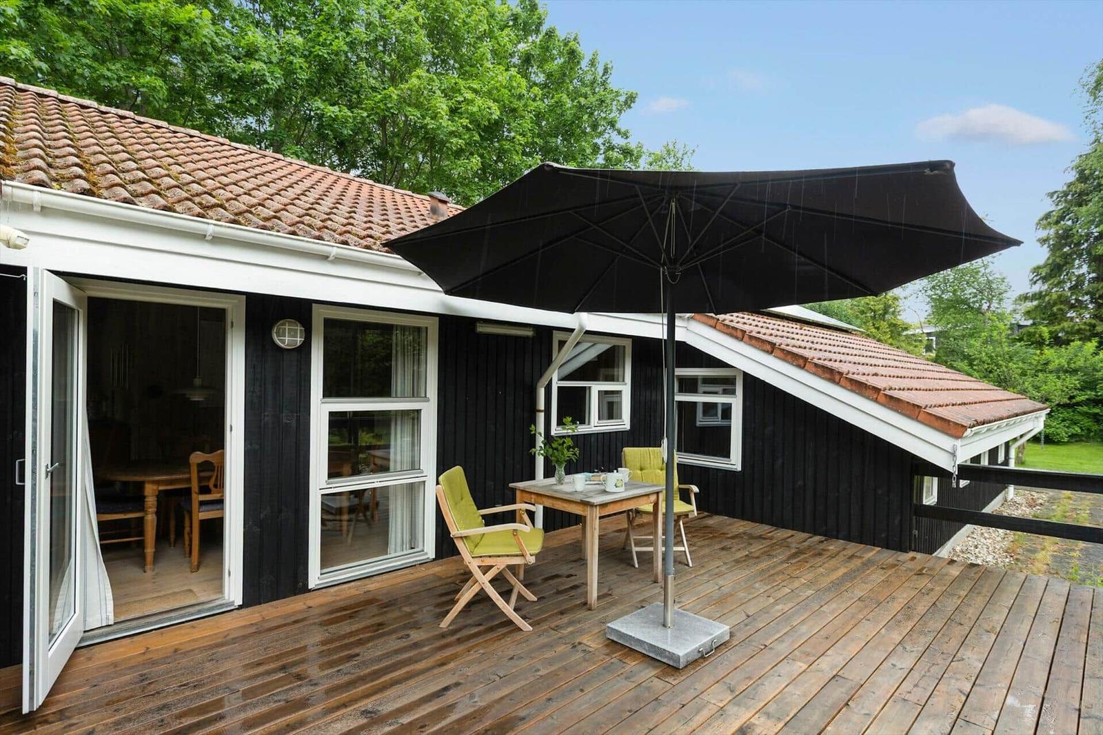 Deck with table, two chairs, and umbrella in front of a house with wooden porch.