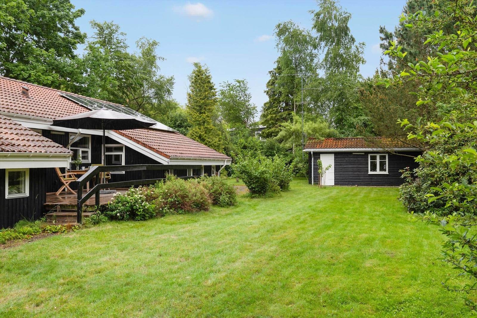 Black wooden house with terrace and large lawn in greenery.