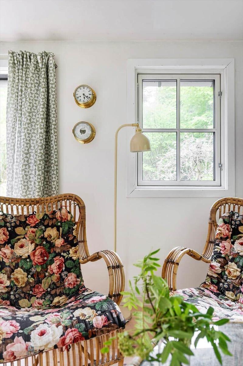 Zwei Rattan-Stühle mit floralen Bezügen stehen vor einem Fenster mit grünem Blick.
