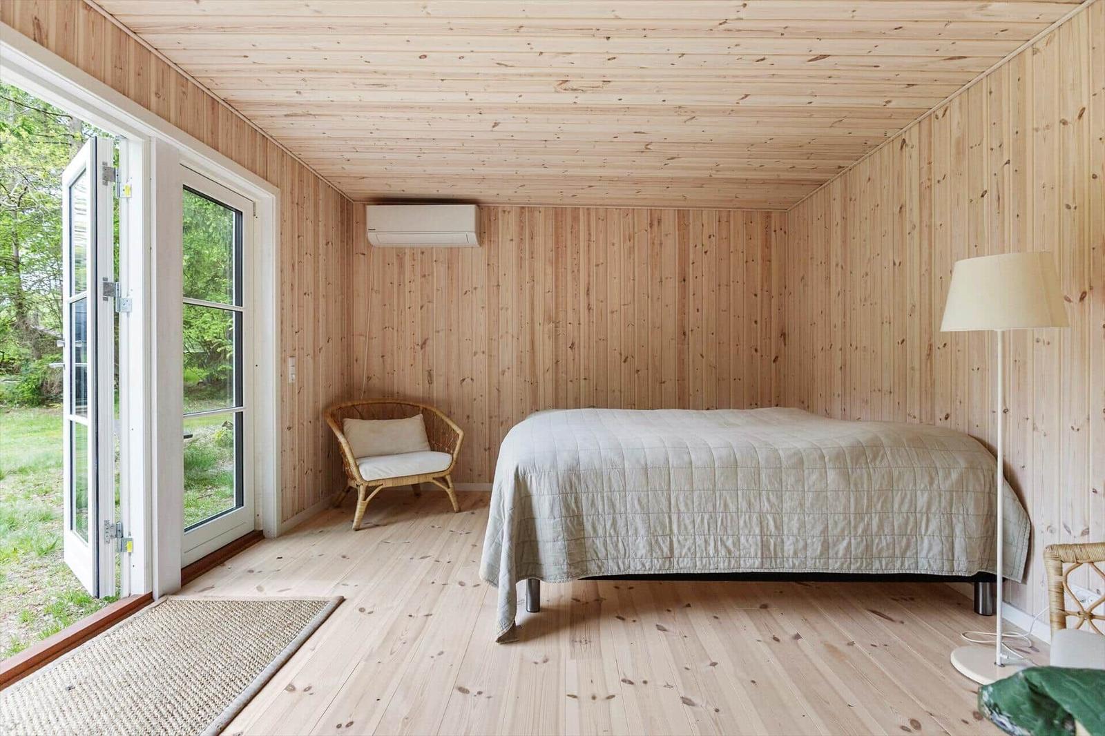 Schlafzimmer mit Holzwand, Bett, Stuhl und Fenster zur Außenseite.