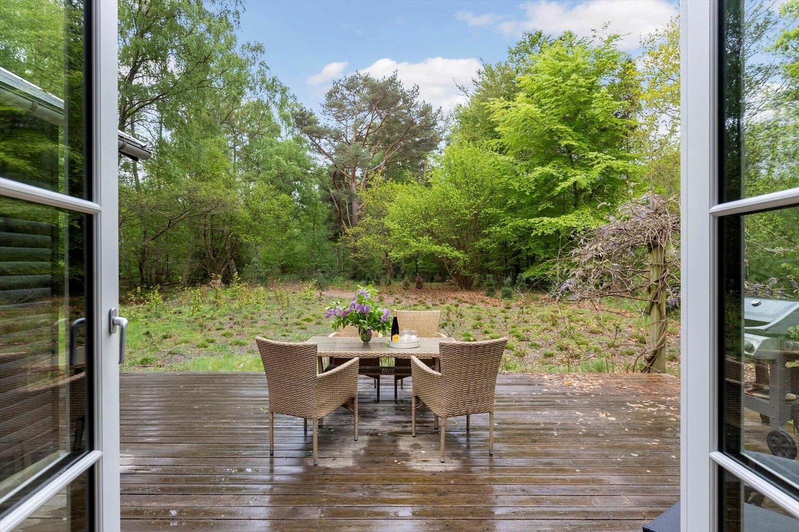 Terrasse mit Tisch und Stühlen, Blick in einen grünen Wald.
