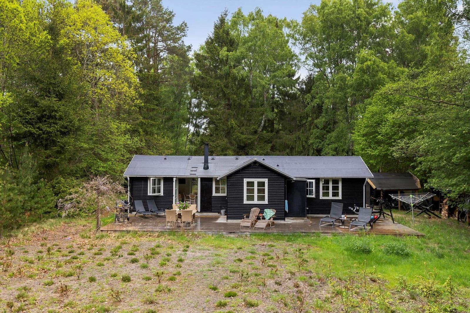 Schwarze Holzhütte mit Terrasse, Garten und umgeben von Bäumen.