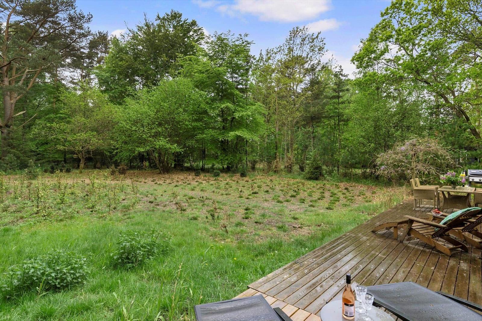 Holzterrasse mit Liegestühlen und Blick in einen grünen Wald.
