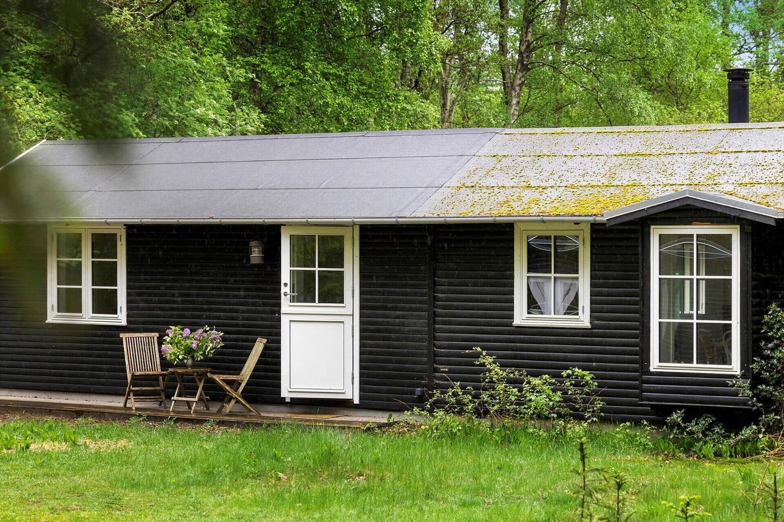 Schwarzes Holzhaus mit weißer Tür und Fenstern, Garten und Tisch mit Stühlen.