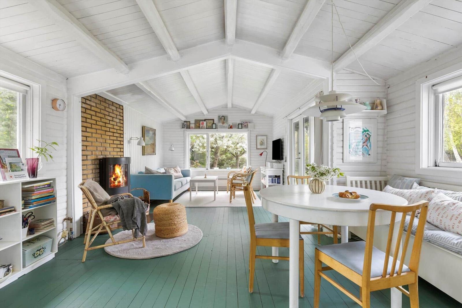 A room with green floor, white ceiling, and wooden furniture. It has a fireplace, a table, and windows.