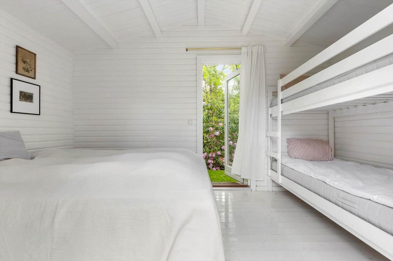 Room with double bed and bunk bed, door to garden with flowers.